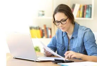 Une femme devant son PC avec une calculette