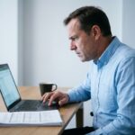 Homme d'affaires examinant attentivement un document signé en ligne sur son ordinateur portable, l'air préoccupé face à une possible erreur