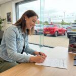 Jeune femme souriante signant un contrat de leasing dans un concessionnaire