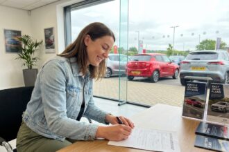 Jeune femme souriante signant un contrat de leasing dans un concessionnaire