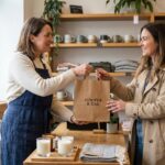 Commerçante remettant un sachet avec logo imprimé à une cliente dans une boutique indépendante
