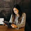 woman wearing white dress shirt using holding black leather case on brown wooden table